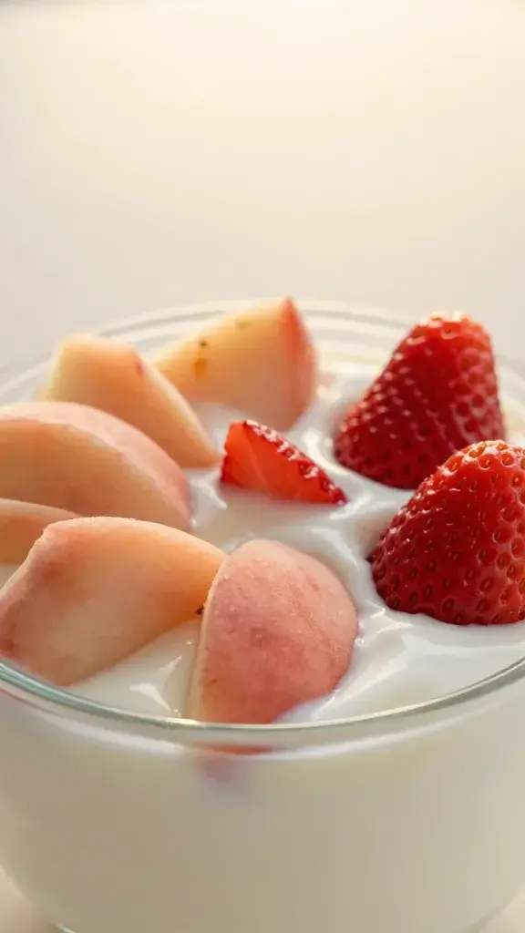 Closeup peach strawberry yogurt bowl in glass, sunrise lighting
