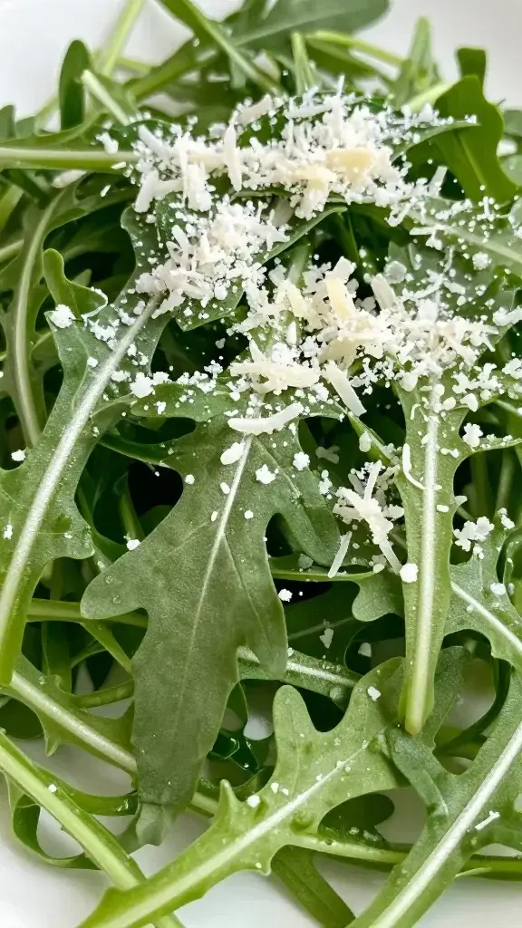 Closeup of grated Parmesan snow atop fresh arugula leaves