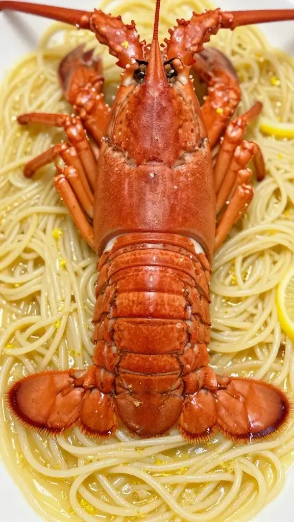 closeup of lobster tail resting on silk pasta strands with lemon zest