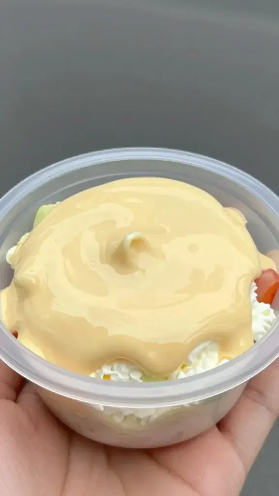 closeup of one portable Mac Salad Cup held in hand, glossy dressing close-up