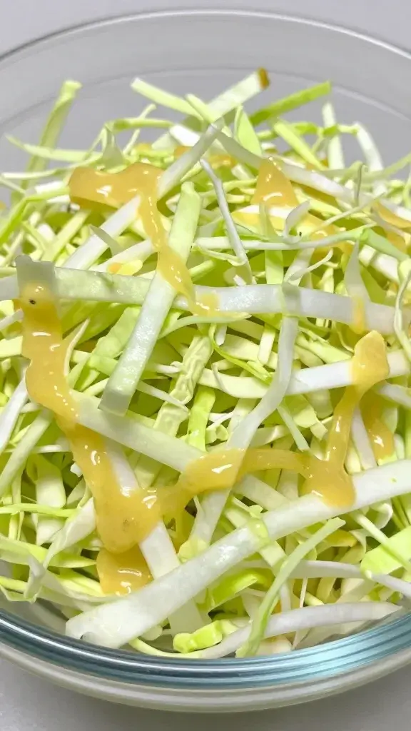Closeup of vibrant shredded cabbage with lime dressing drizzle on glass bowl