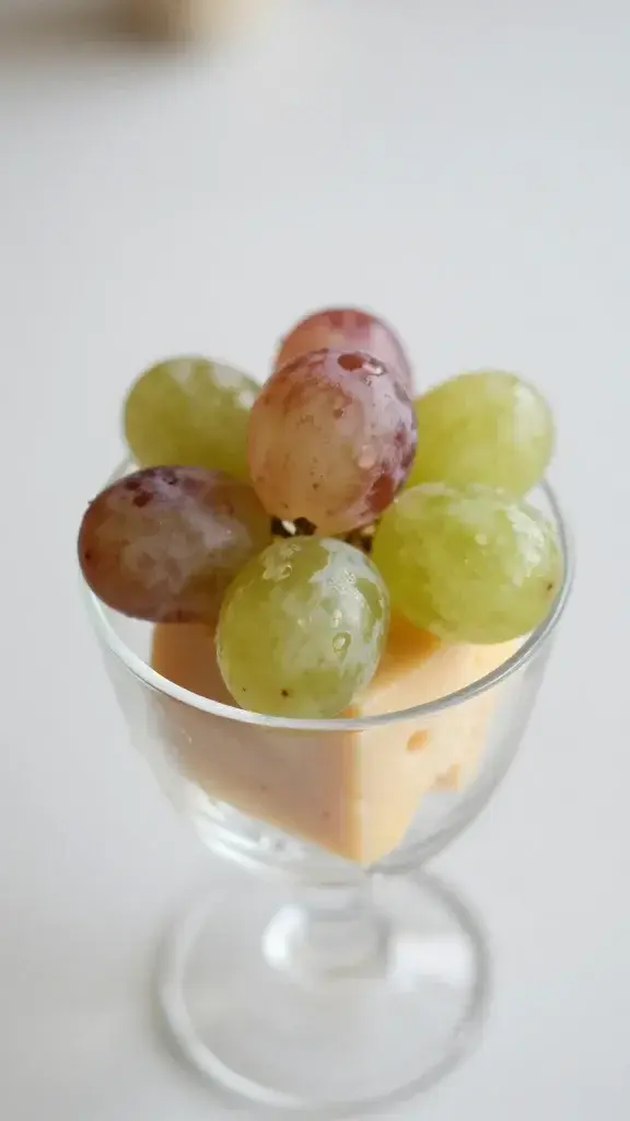 closeup of a single grape-and-cheese bite in a clear cup, soft natural light
